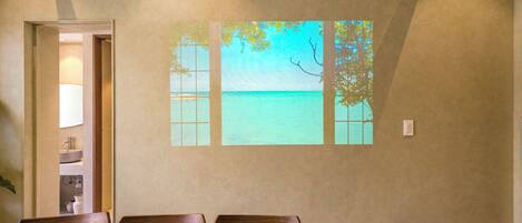 A dining area with a wooden table and chairs, a view of the sea through a window, and a door leading to a bathroom.
