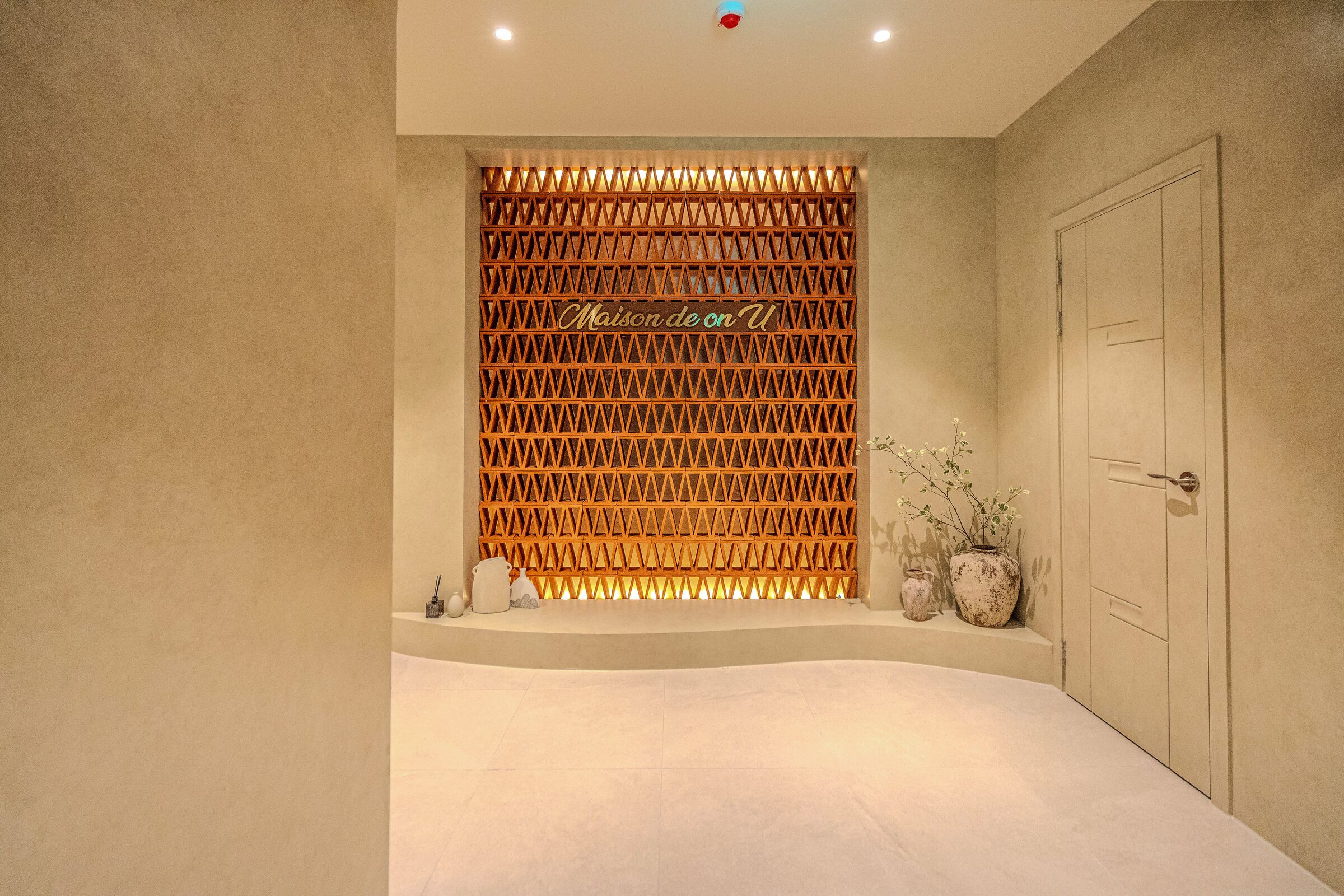 Una habitación de hotel moderna con un panel de pared de madera celosía, una cama grande y una puerta a la derecha.