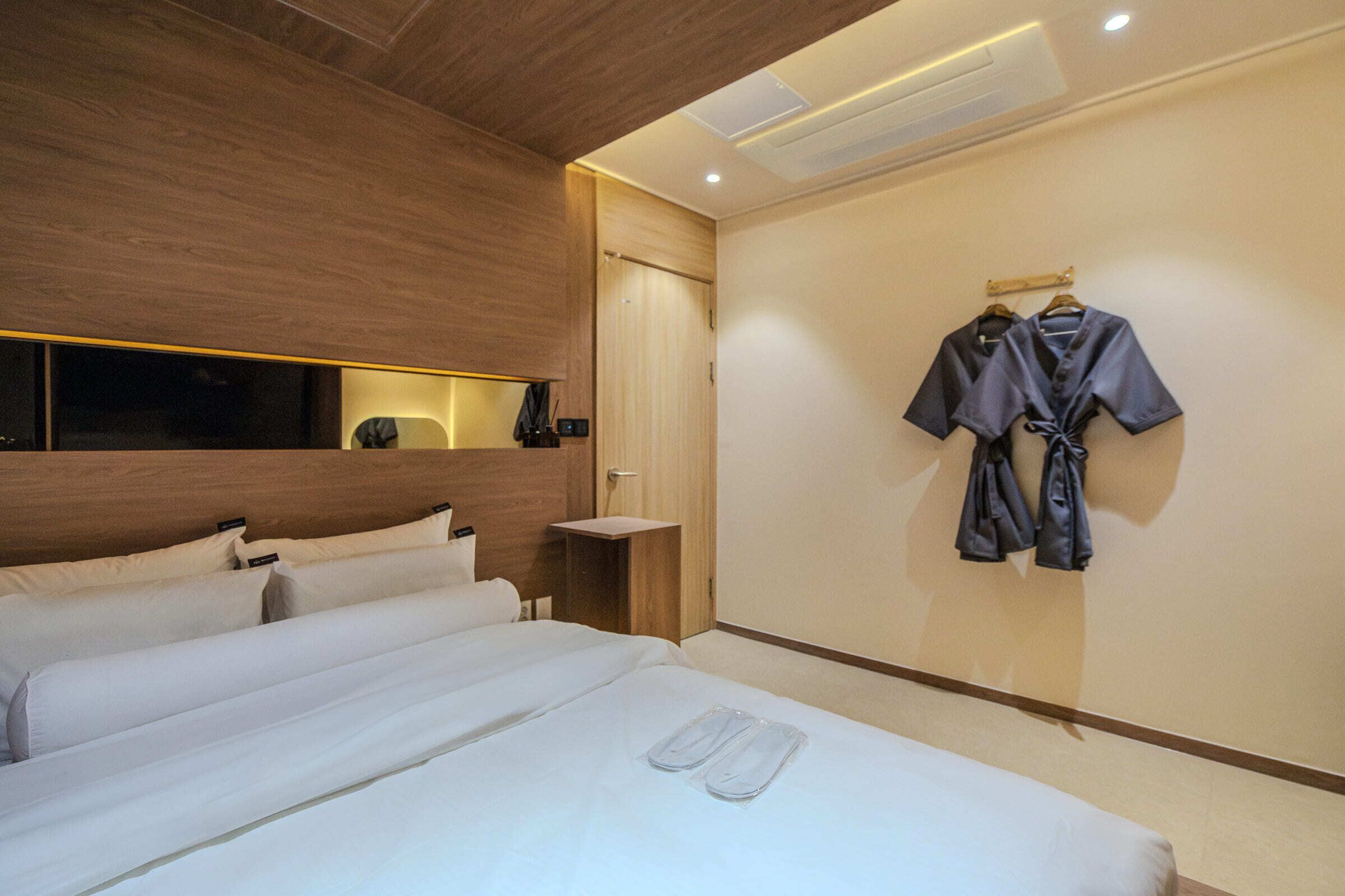 Habitación de hotel con una cama grande, cabecera de madera, mesita de noche y perchero en la pared.