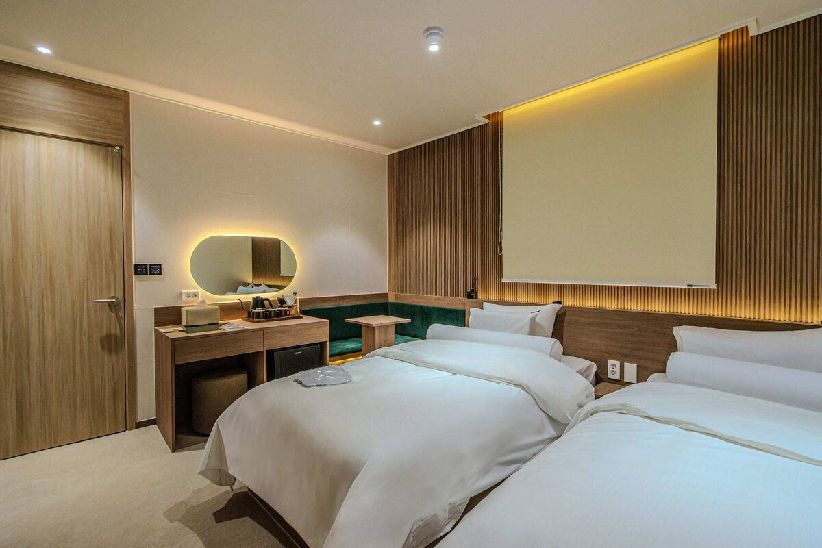 A hotel room with a large bed, a desk with a mirror, a small table, and a green accent wall.