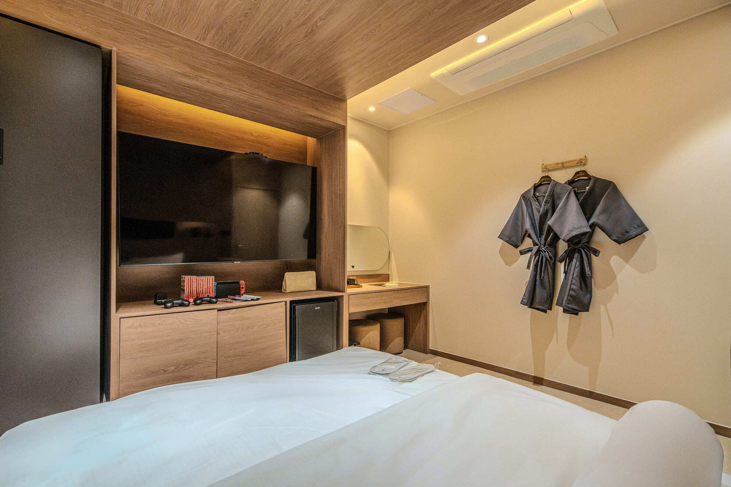 A hotel room with a bed, a desk with a computer, a mirror, and a wall-mounted robe rack.