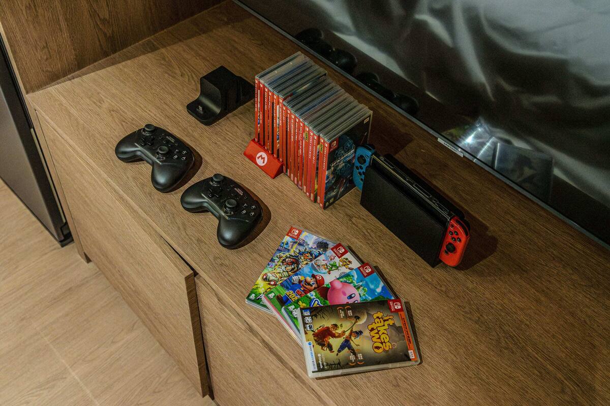 A wooden table with video game controllers, a Nintendo Switch, and a collection of video game cases.