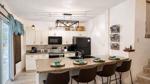 A modern kitchen with white cabinets, a stainless steel oven, a black refrigerator, and a granite countertop. There are four bar stools and a small island with a sink. - Escape to Tranquility at Mountain Top Condo! (Somerset)