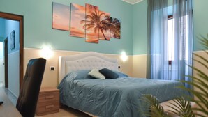 A bedroom with a bed, bedside table, and a wall with three palm tree paintings. - "Enchanted Home" Independent and close to the center of Civitavecchia- Rome (Civitavecchia)