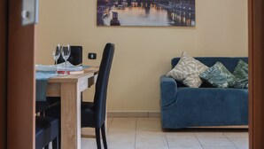 A dining area with a table set for two, a blue sofa, and a wall-mounted painting. - "Enchanted Home" Independent and close to the center of Civitavecchia- Rome (Civitavecchia)