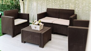 A wicker sofa set with a matching ottoman and side chairs, arranged on a patio with a green hedge and white curtains in the background. - "Enchanted Home" Independent and close to the center of Civitavecchia- Rome (Civitavecchia)