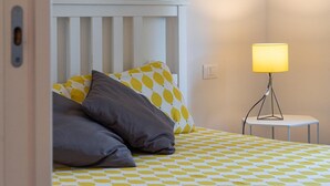 Un lit avec une couvre-lit à motifs, deux oreillers, une lampe de chevet et une tête de lit blanche.