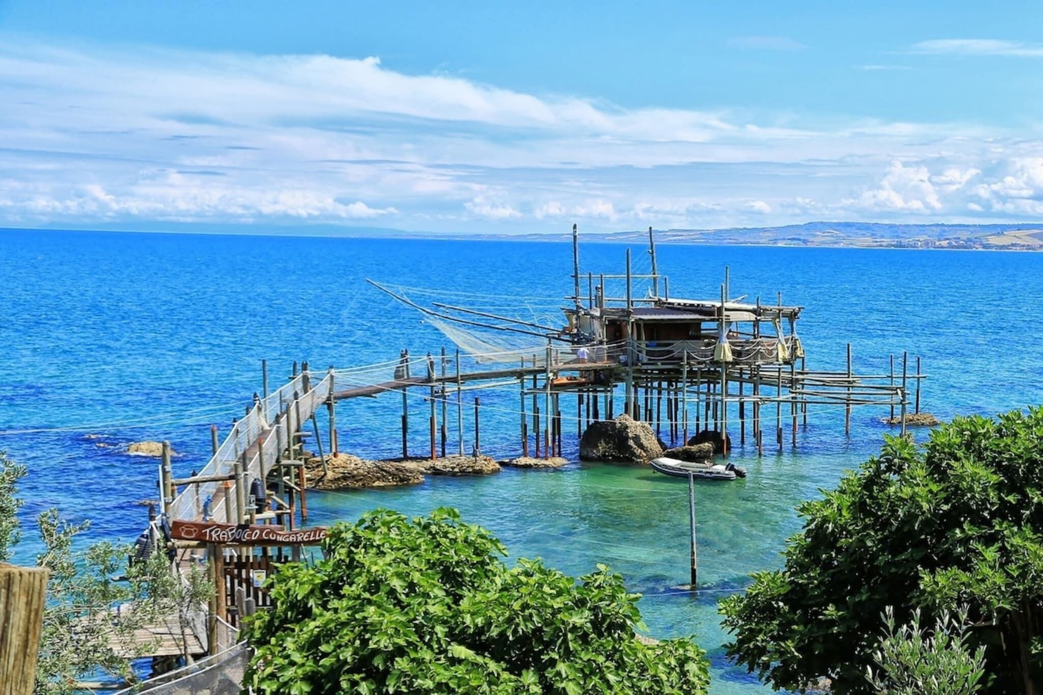 Un muelle de madera se extiende hacia un mar azul y transparente, con un pequeño bote amarrado al final.