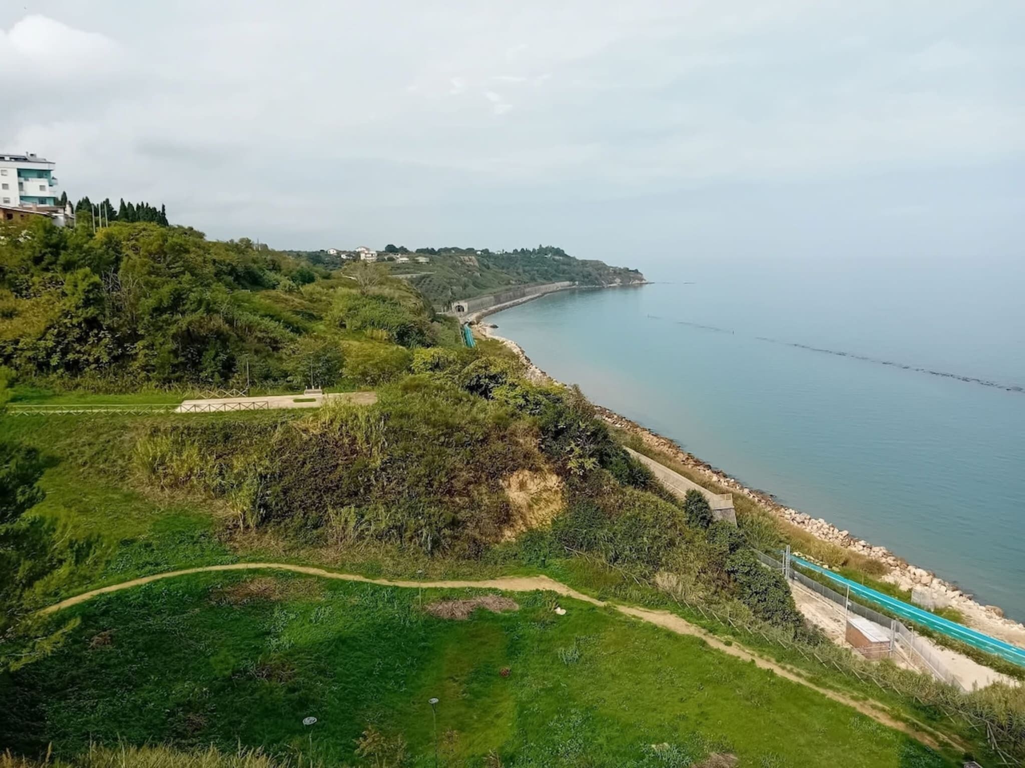 Paesaggio costiero con un sentiero pedonale, un ponte e una costa in lontananza.