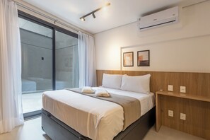 Une chambre d’hôtel comprenant un lit, une porte-fenêtre coulissante, un appareil de climatisation et une table de chevet en bois.