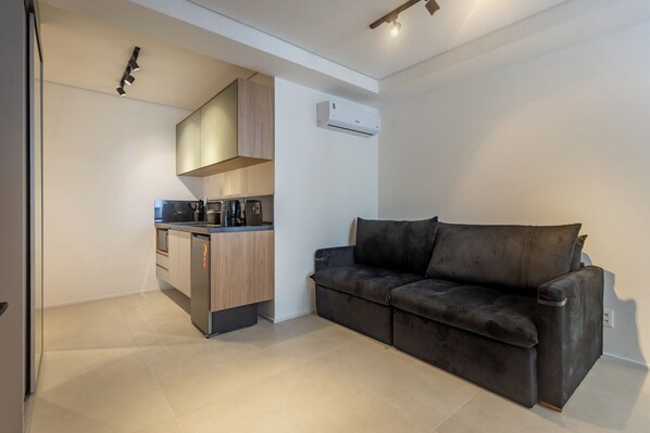 A compact living space with a kitchenette, a sofa, and a ceiling-mounted air conditioner. - 360 Diamond Jardins (Sao Paulo)
