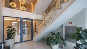 Un hall d’hôtel moderne avec une entrée dotée d’une porte en verre, un escalier et des plantes en pot.