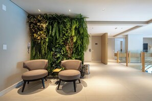 A modern interior with two beige chairs, a wall-mounted plant display, and a clean, minimalist design. - 360 Diamond Jardins (Sao Paulo)