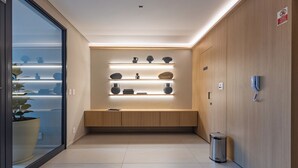 Un hall d’hôtel moderne avec un comptoir d’accueil en bois, un mur en verre orné d’une plante en pot et un téléphone fixé au mur.