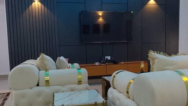 Una sala de estar moderna con televisor de pantalla plana, dos sofás blancos con detalles dorados, una mesita de centro y una iluminación ambiental.