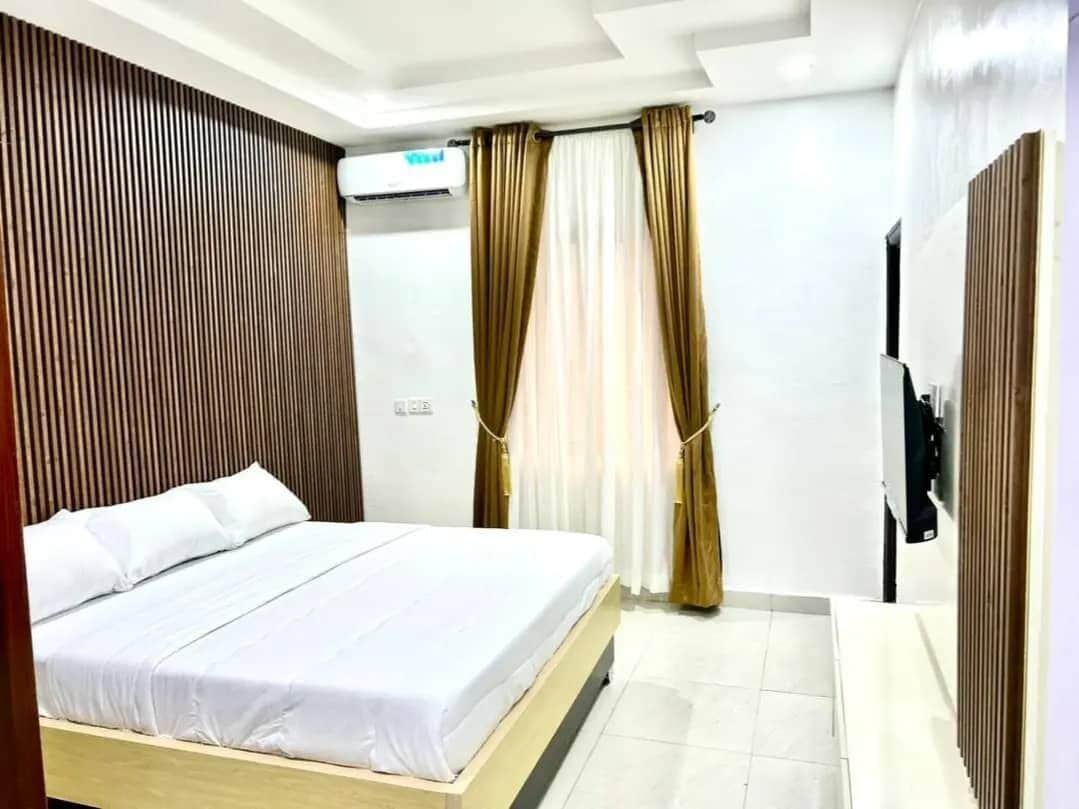A hotel room with a bed, curtains, a TV, and a wooden panel wall.