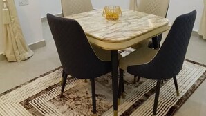 Un comedor con una mesa, cuatro sillas, un tapete estampado y un cuadro en la pared.