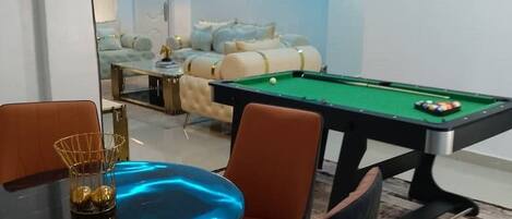 A modern living room with a pool table, a sofa, and a dining area with chairs.