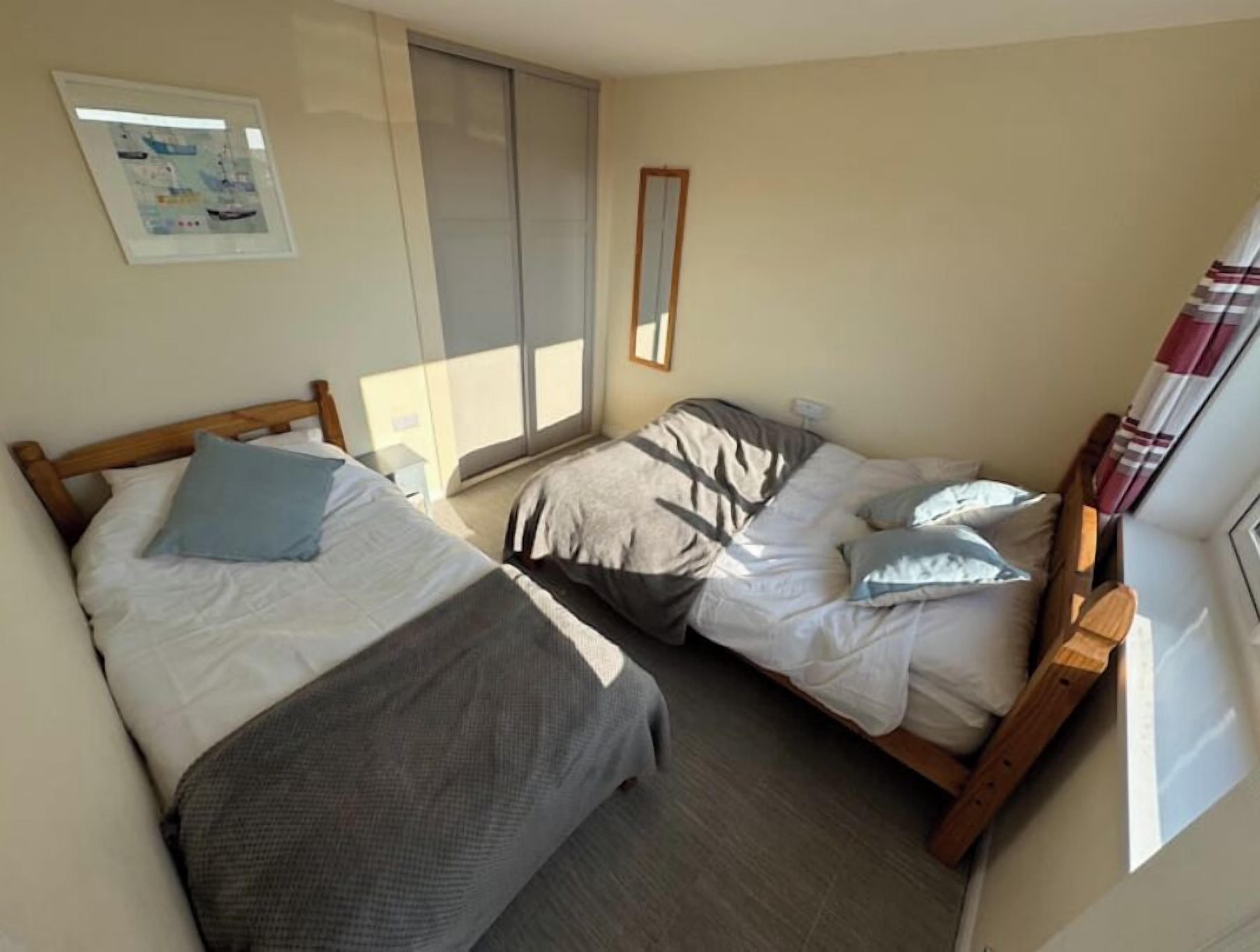 A bedroom with two single beds, a window with blinds, a framed picture on the wall, and a wooden headboard.