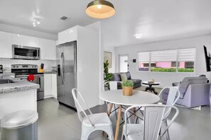 A modern kitchen with white cabinets, stainless steel appliances, and a dining area with white chairs and a round table.