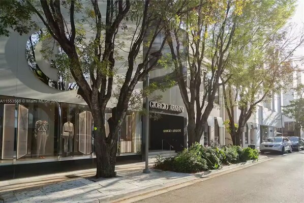 A storefront with a large tree in front, a sidewalk, and parked cars.