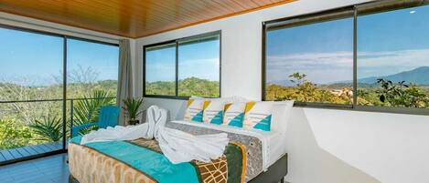 A bedroom with a large bed, two windows, and a view of a landscape.