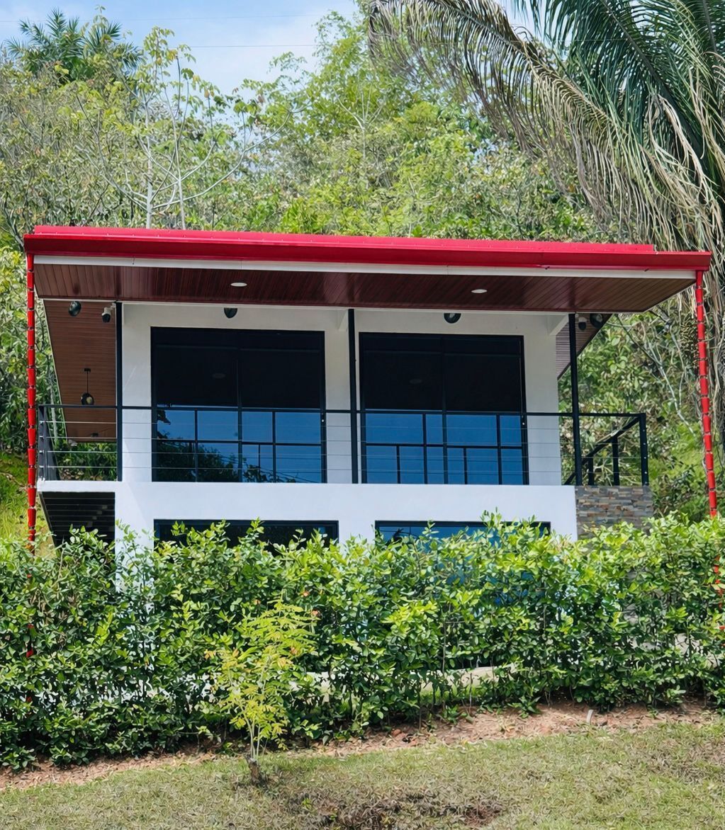 Un bâtiment à deux étages, doté d’un toit rouge, de grandes fenêtres et entouré d’une végétation luxuriante.