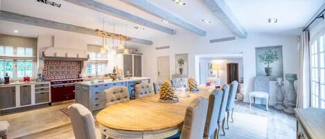 A spacious dining area with a wooden table and upholstered chairs, a kitchen with modern appliances, and a large window providing natural light.