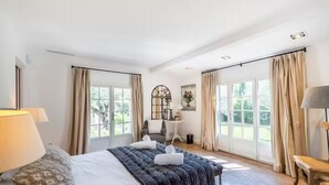 A spacious bedroom with a large bed, two windows with curtains, a small table with a lamp, and a chair. - Magnificent Villa near Fayence (Saint-Paul-en-Forêt)