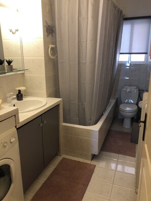 Compact bathroom with sink, toilet, shower, and washing machine for convenient laundry facilities.