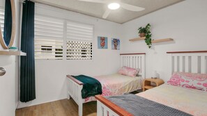 Un dormitorio con dos camas individuales, una ventana con persianas, un ventilador de techo y estantes empotrados con objetos decorativos.