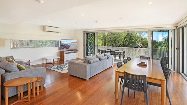 A spacious living area with a grey sofa, wooden coffee table, and a dining table with chairs. - Hume Parade 19, Unit 1, Currimundi (Currimundi)