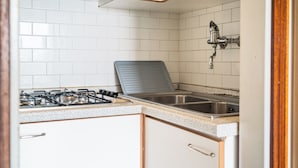 A kitchen with white tiled walls, a gas stove, a sink, and wooden cabinets.
