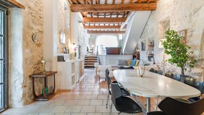 Un comedor amplio con una mesa y sillas de mármol, una escalera que conduce a un nivel superior y una pared de piedra rústica.