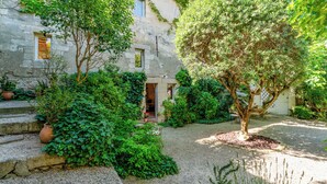 Un edificio de piedra con un patio de grava, rodeado de abundante vegetación y plantas en macetas.