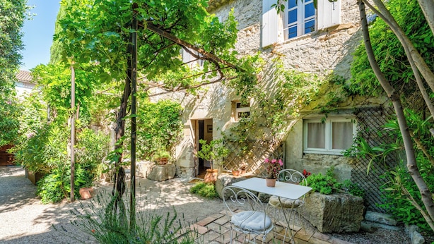 Una casa de piedra con un patio jardín, una mesa con sillas y plantas en macetas.