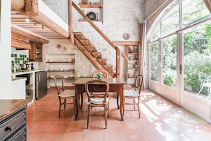 A rustic kitchen with wooden beams, a dining table with chairs, and a staircase leading to an upper level. - Le Clos des Chartreux (Villeneuve-lès-Avignon)