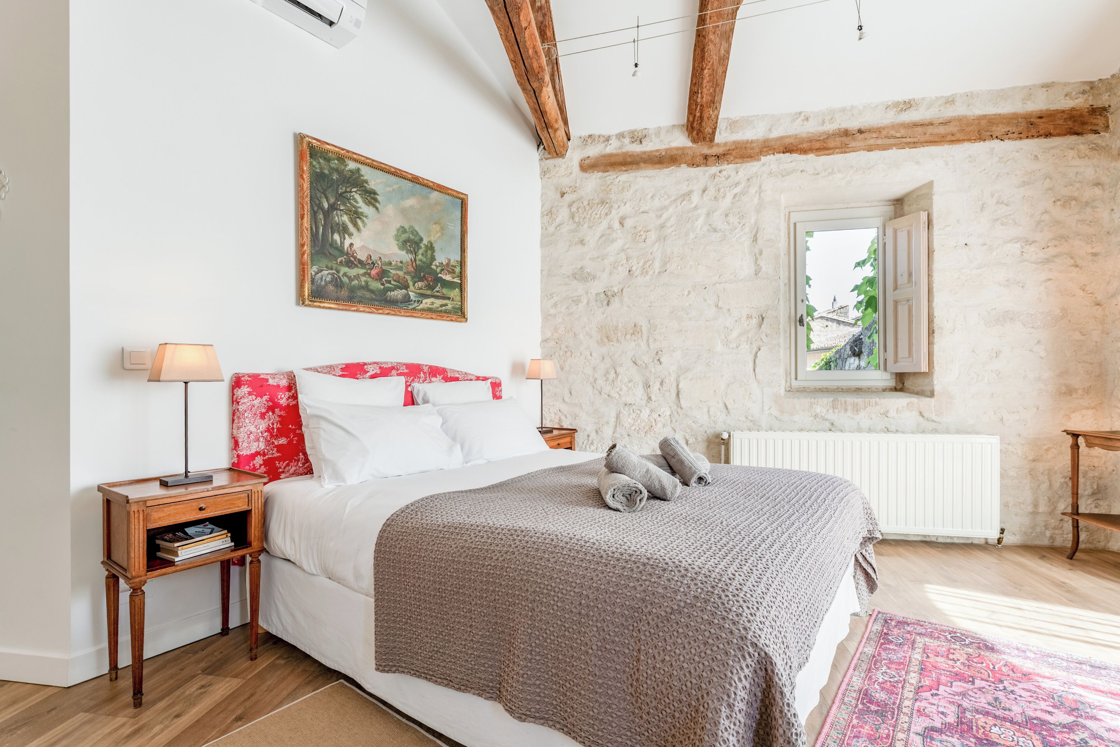 A bedroom with a bed, nightstands, a window, a radiator, and a painting on the wall.