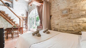 Un dormitorio con pared de piedra, escalera de madera, cama con ropa blanca y vistas a través de una ventana.