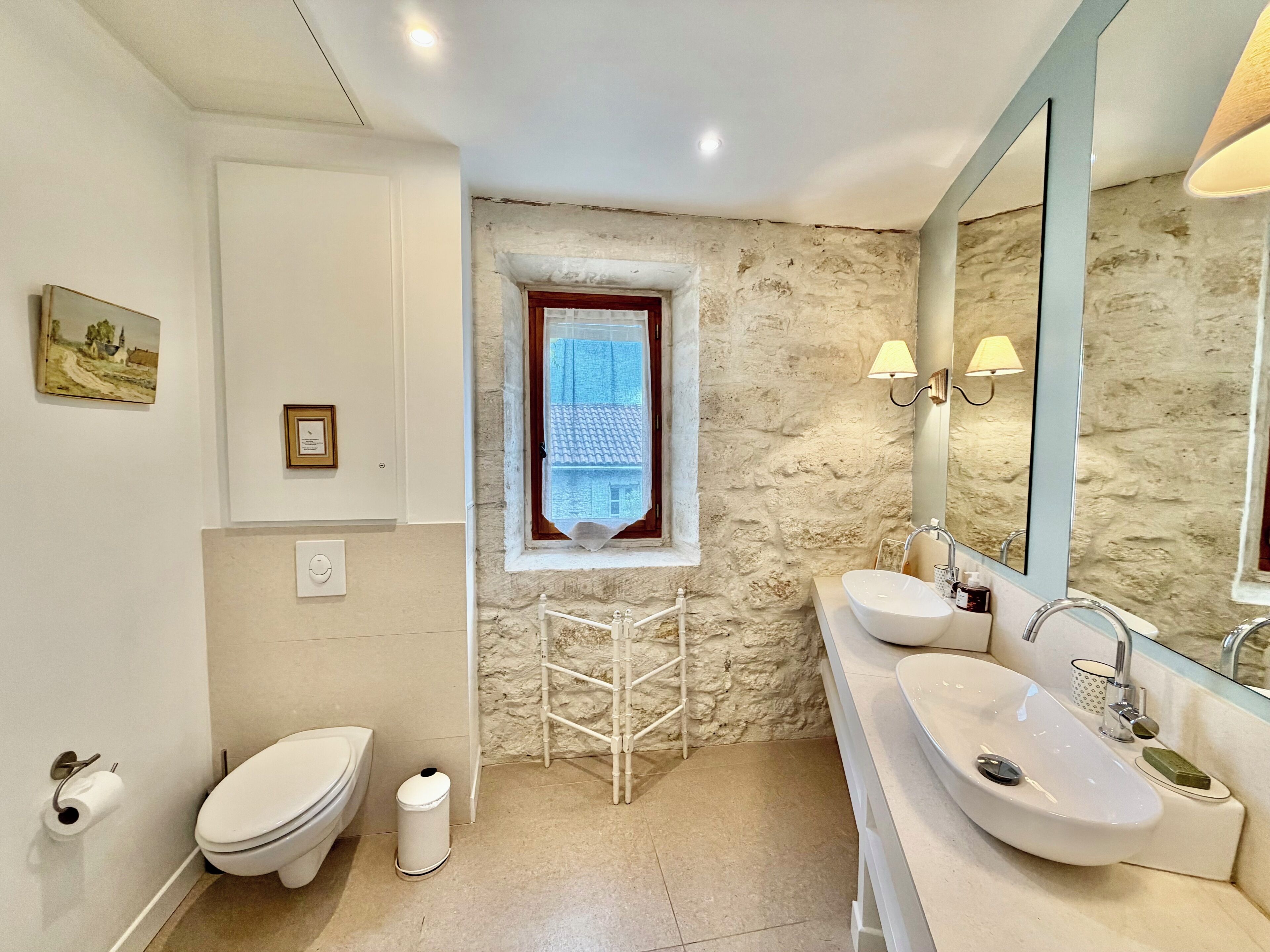 A bathroom with a toilet, sink, mirror, and a window with a view of a building.