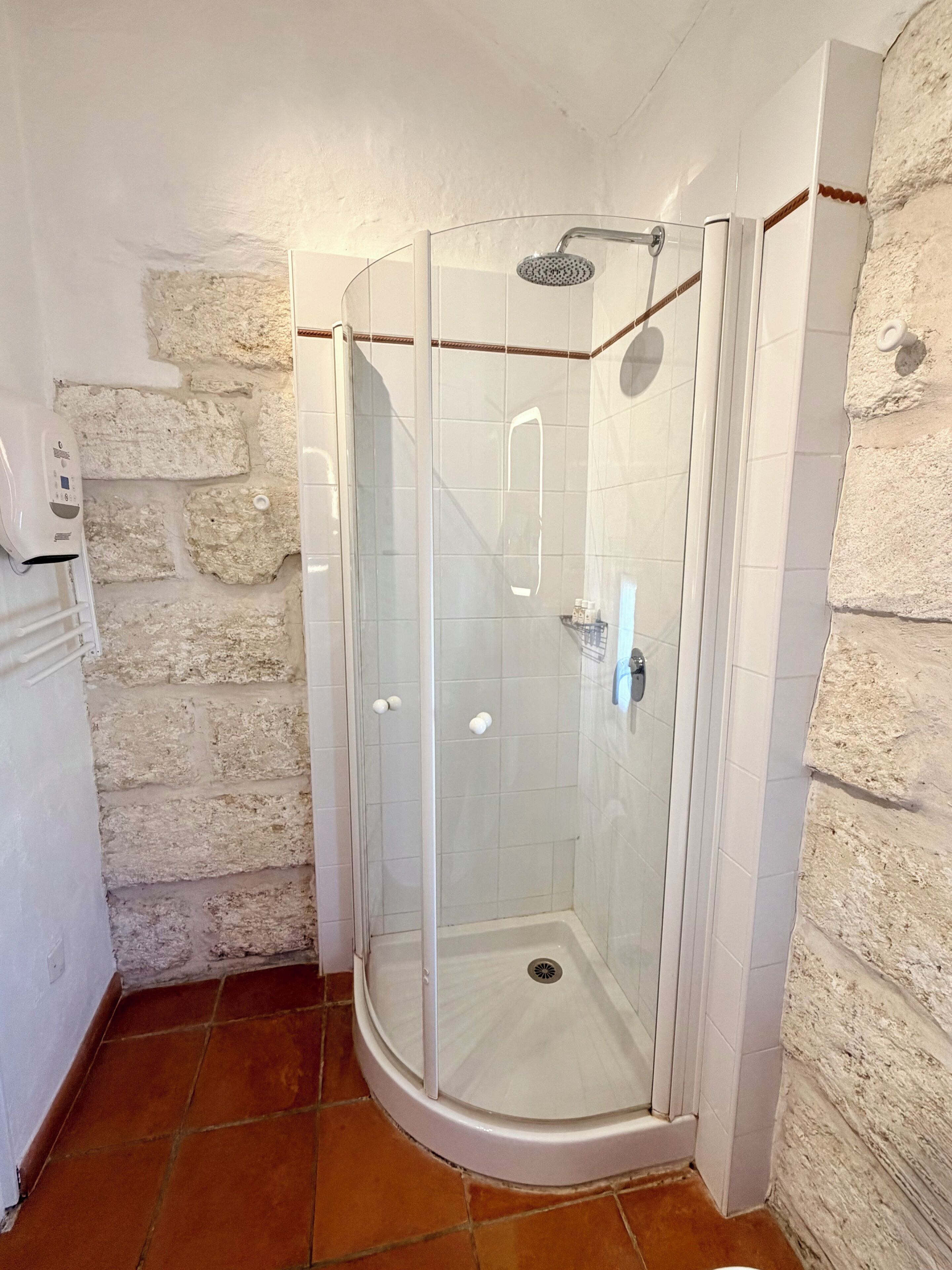 Un box doccia in vetro con soffione, una parete rivestita di piastrelle bianche e una parete in pietra.