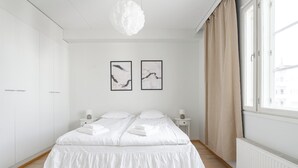 A bedroom with a bed, two bedside tables, a hanging light fixture, a window with curtains, and two wall-mounted pictures. - Lakefront Home near Downtown (Jyväskylä)