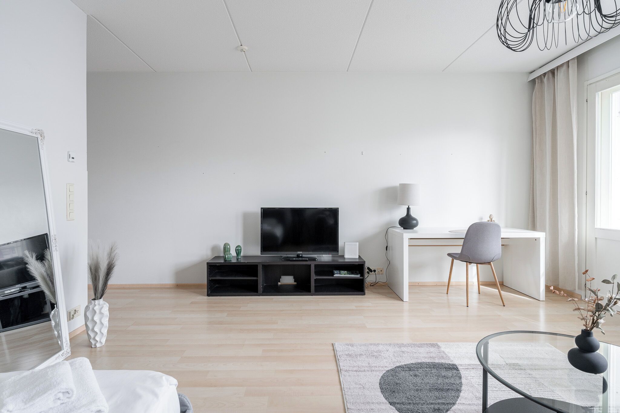 A modern living room with a flat-screen TV, a desk, a chair, and a glass coffee table.