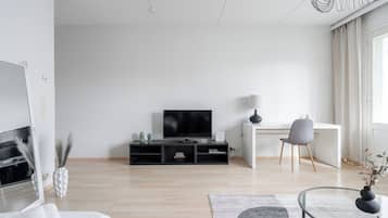 A modern living room with a flat-screen TV, a desk, a chair, and a glass coffee table.