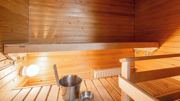 A sauna room with wooden walls and benches, a metal bucket, and a radiator. - Lakefront Home near Downtown (Jyväskylä)