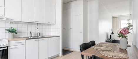 Una cocina moderna con armarios blancos, una mesa de comedor de madera con sillas negras y una lámpara colgante.