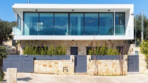 A modern two-story building with large glass windows, stone facade, and a gated entrance. - White View Villa by Alex – Your Dream Holiday in the Heart of Crete (Chania)