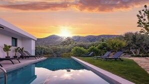 A swimming pool with lounge chairs, a modern building, and a mountainous landscape in the background. - White View Villa by Alex – Your Dream Holiday in the Heart of Crete (Chania)