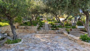 A stone pathway leading through a garden with trees and plants. - White View Villa by Alex – Your Dream Holiday in the Heart of Crete (Chania)