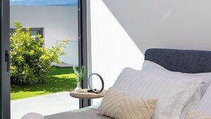A bedroom with a bed, pillows, a bedside table with a mirror, and a view of a snowy mountain through a large window. - White View Villa by Alex – Your Dream Holiday in the Heart of Crete (Chania)